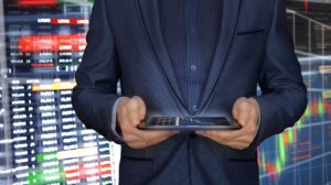 a stock trader holding a mobile phone in front of stock charts